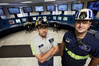 Two men in hard hats standing in a control room